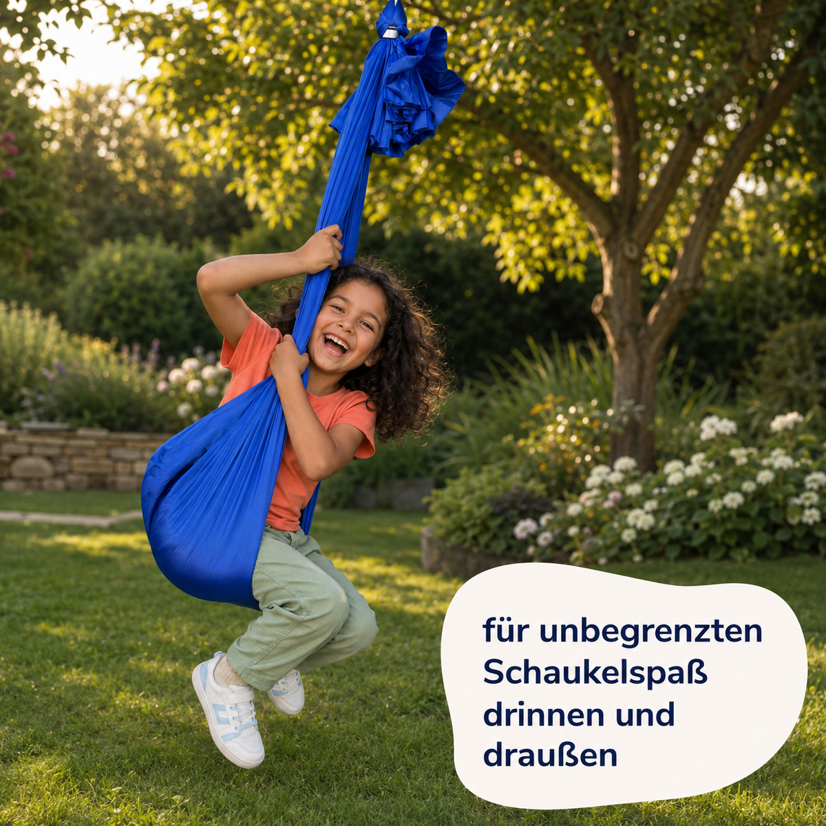 Mädchen schwingt lachend im royalblauen Tuch, im Garten an einem Baum aufgehängt