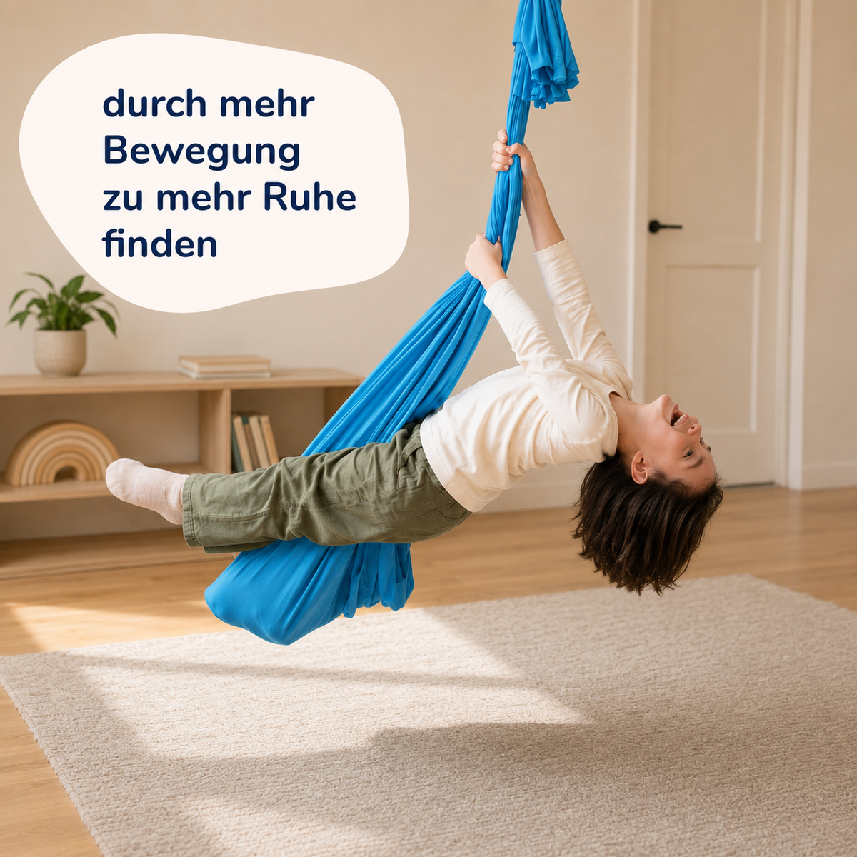 Kind hängt kopfüber im türkisfarbenen Tuch und streckt die Beine, Wohnzimmer